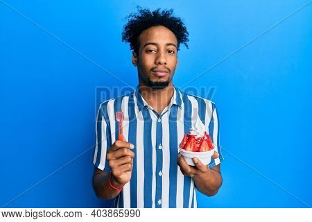 Young african american man with beard eating strawberry ice cream relaxed with serious expression on face. simple and natural looking at the camera. 