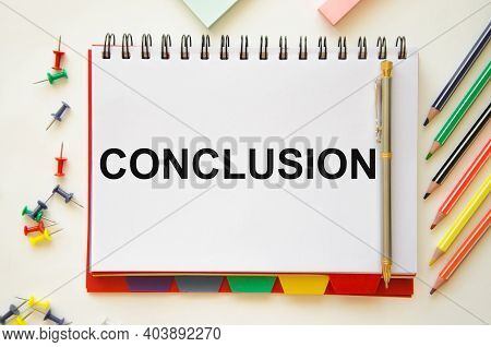 The Word Conclusion Is Written On A White Notebook That Lies On A White Table Near Stickers And Colo