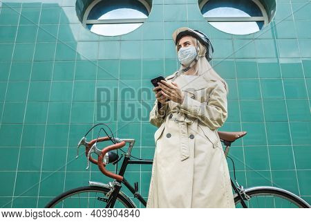 Woman in protective mask, in helmet using her smartphone device. Girl standing on green background. Mood Boosting Color.