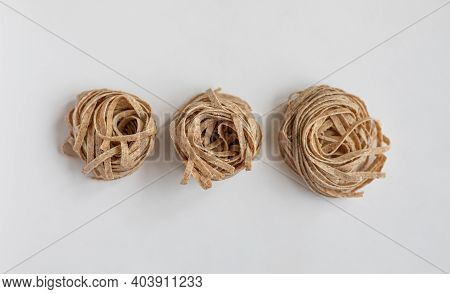 Raw Whole Grain Brown Pasta On A White Background. Delicate Wholemeal Pasta Made Of Graham Flour, Ri