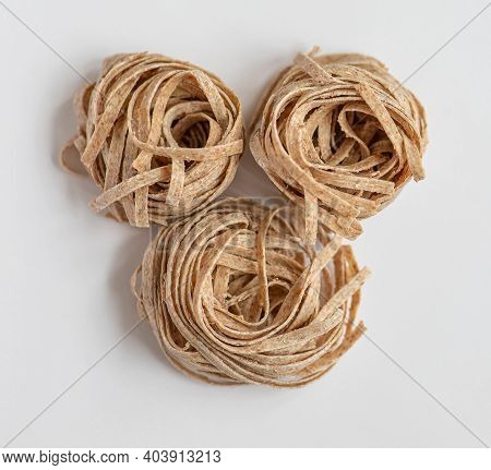 Raw Whole Grain Brown Pasta On A White Background. Delicate Wholemeal Pasta Made Of Graham Flour, Ri