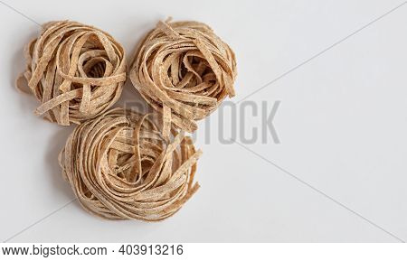 Raw Whole Grain Brown Pasta On A White Background. Delicate Wholemeal Pasta Made Of Graham Flour, Ri