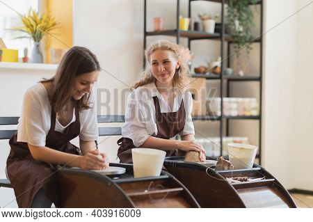 Two Women Make Pottery On A Pottery Wheels, Shaping Clay By Their Hands, Close Up. Pottery Craft Wor