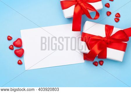 Valentines day greeting card template. Gift boxes and heart candy sweets over blue background. Top view flat lay with copy space