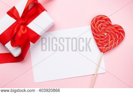 Valentines day greeting card template. Gift box and heart candy lollipop over pink background. Top view flat lay with copy space