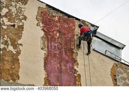 Working Steeplejack With Special Equipment Repairs The Facade Of The Building. House Walls Cleaning 