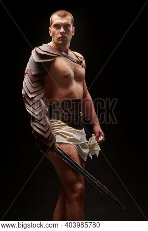 Gladiator With Sword And Armor On A Black Background. A Warrior In Gladiatorial Armor With A Sword I