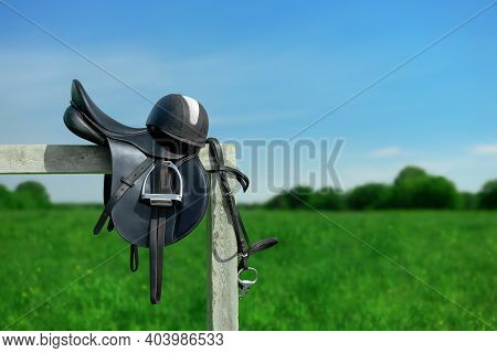 The Bridle, The Horse Saddle And The Riding Helmet Are On The Wooden Hitching Post In Outdoors.