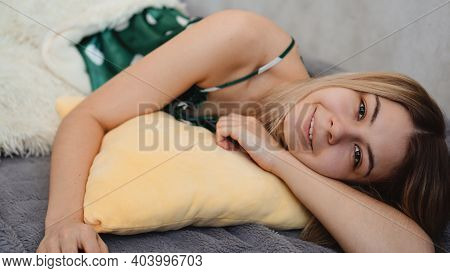 Young Beautiful Girl Woke Up At Home. She Lies On A Yellow Pillow And Is Covered With A White Blanke