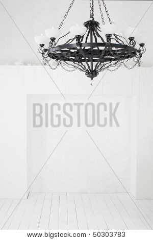 Vintage black chandelier with candles in an empty room with white walls and floors