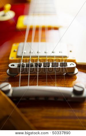 Red sunburst color single cutaway electric solid body guitar. Focus on bridge. Shallow depth of field. 