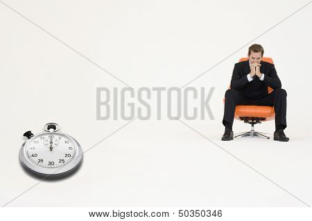 Anxious businessman sitting on chair with stopwatch showing time representing loss of time