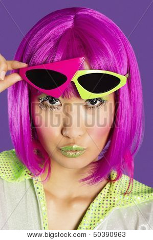 Portrait of young funky woman in pink wig puckering lips over purple background