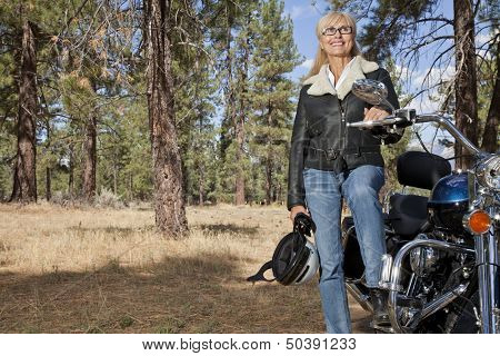 Senior woman poses with motorcycle in forest