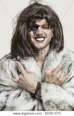 Portrait of young man with painted face making rebellious gestures over gray background