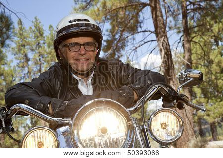 Senior man wearing helmet leaning on motorcycle handlebars in forest