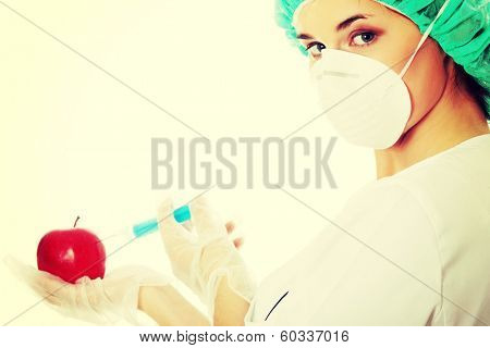 Woman in white coat with syringe and apple (biotechnologist). White background. Studio shot.