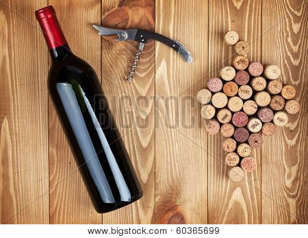 Red wine bottle, corkscrew and grape shaped corks on wooden table background