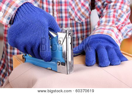 Fastening fabric and wooden box using construction stapler on bright background