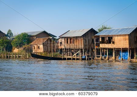 Traditional Stilts House And Long Boats In Water Under Blue Sky