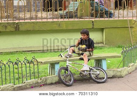 Boy Eating on Bench in Banos, Ecuador