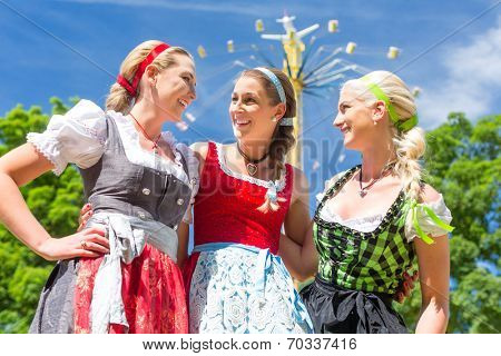 Women friends visiting Bavarian folk festival in  Dirndl standing in front of carousel 