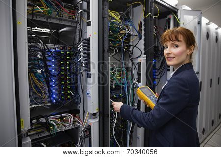Happy technician using digital cable analyzer on server in large data center