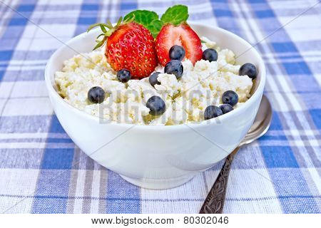 Curd in bowl with strawberries and blueberries on tablecloth