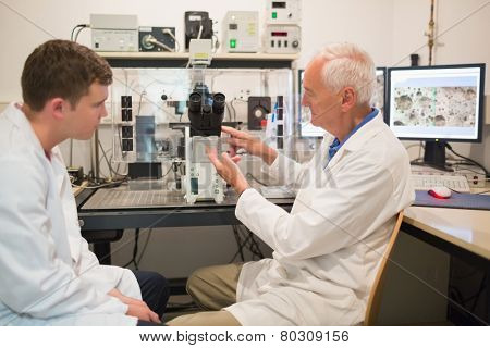 Biochemist using large microscope and computer with student at the university