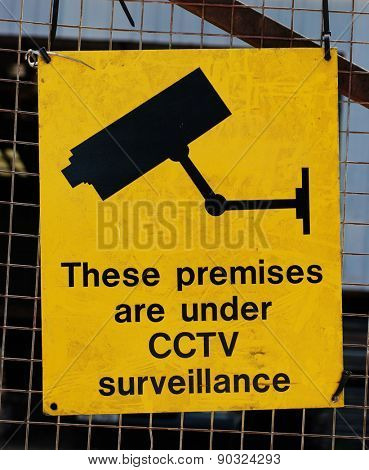 Yellow warning sign for CCTV surveillance using security cameras to secure a premises against crime on a wire mesh fence
