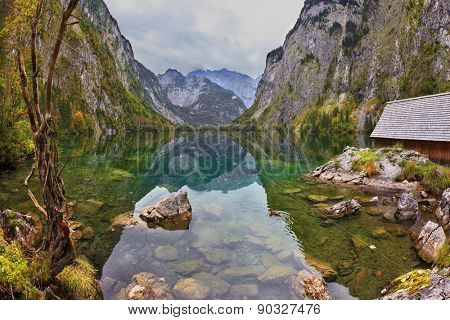 Magic reflection in German lake Koenigssee. Cloudy day on the lake. Clouds and mountains reflected in the mirrored surface of the water