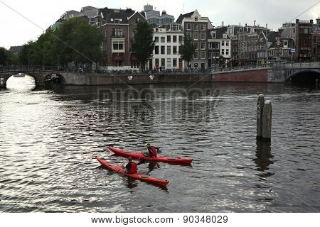 AMSTERDAM, NETHERLANDS - AUGUST 8, 2012: Two people on canoes training in the Amstel River near the Dutch National Opera in Amsterdam, Netherlands. 