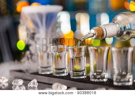 Barman pouring hard spirit into glasses in detail