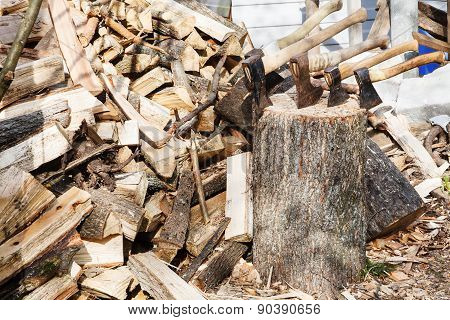 Pile Of Firewoods And Several Axes In Wooden Block