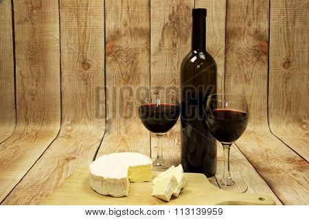 Two Wine Glasses With Red Wine,bottle Of Wine And Cheese On Wooden Table