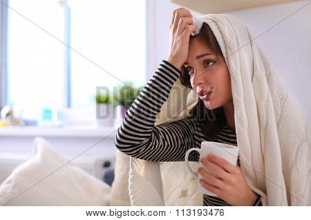 Portrait of a sick woman blowing her nose while sitting on the sofa