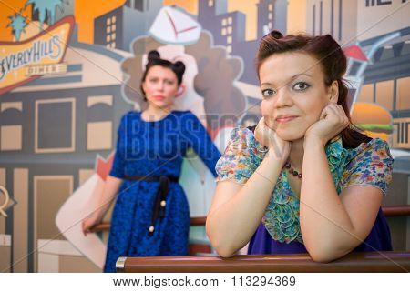 Two women in retro-style dresses at bar with art wall, focus on the right woman.