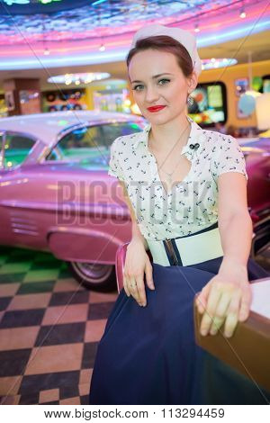 Young woman in retro dress in bar with pink car.