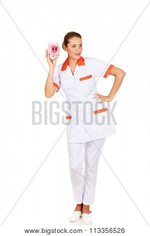 Young beautiful female doctor or nurse holding a piggybank.