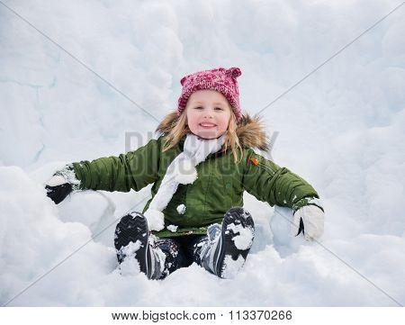 Happy Child In Green Coat Sitting On The Snow