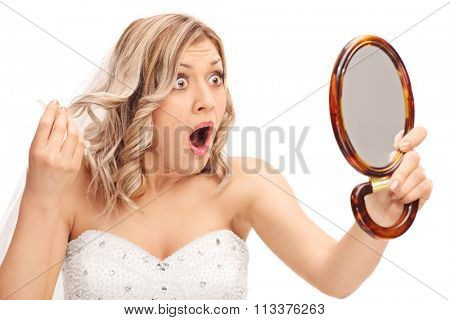 Young enraged bride looking at her hairstyle in a mirror isolated on white background