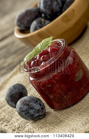 Setting With A Glass Jar Of Plum Marmalade On A Burlap Sac With Two Fresh Plums