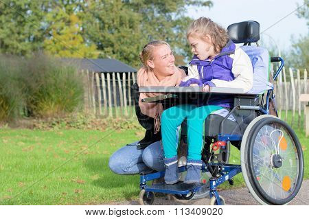 Disability a disabled child in a wheelchair relaxing outside together with a care assistant