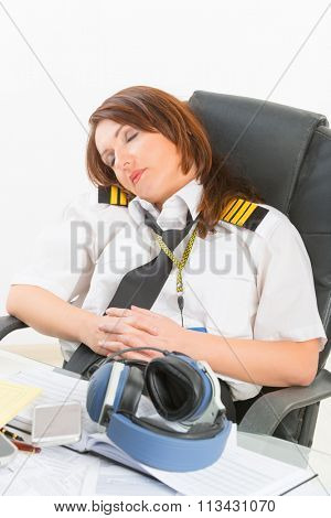 Overworked woman pilot wearing uniform with epaulettes resting or sleeping in briefing room