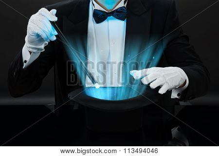 Magician Holding Magic Wand Over Illuminated Hat