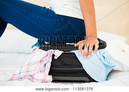 Woman sitting on her overfull suitcase at home