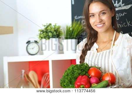 Smiling young woman holding vegetables standing in kitchen