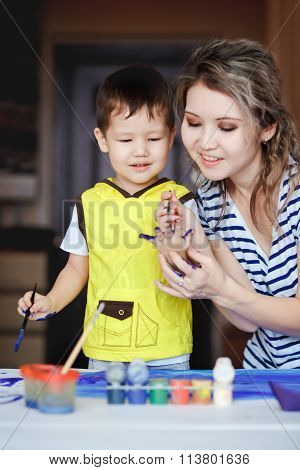 Entertaining childhood, a little boy playing with his mother, draws, paints on the palms. Teaching c