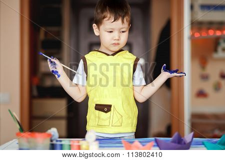 Little boy in a yellow T-shirt stained with paint after the painting does not know what to do.