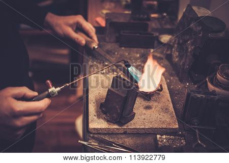 Goldsmith melting gold to liquid state in crucible with gasoline burner.